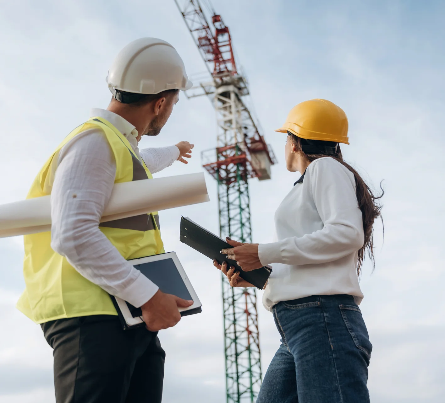 Kierownicy budowy w kaskach nadzorują prace żurawia na placu budowy (Nadzór budowlany)